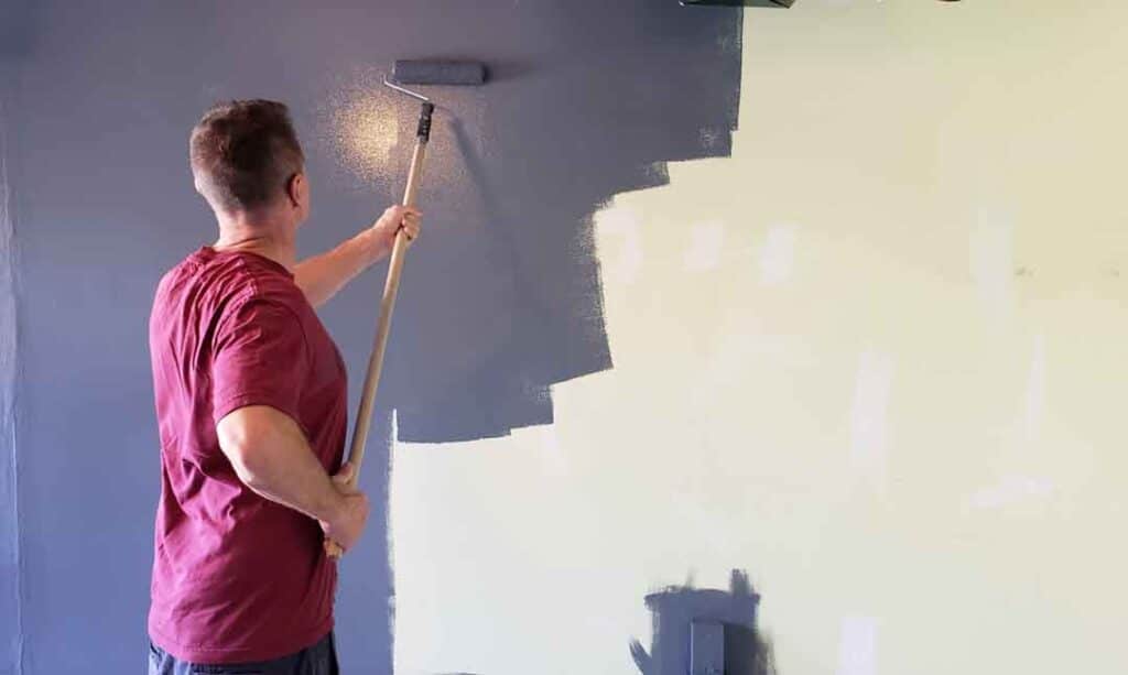 Man Using a Roller to Paint a Wall in Gray